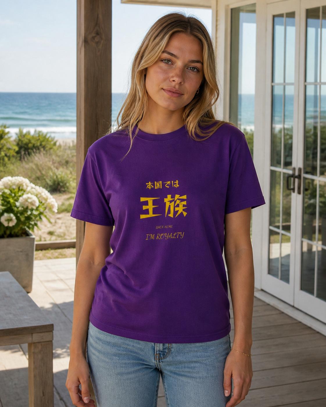 「本国では王族」と刷られた紫のTシャツを着て海辺に立つ人
