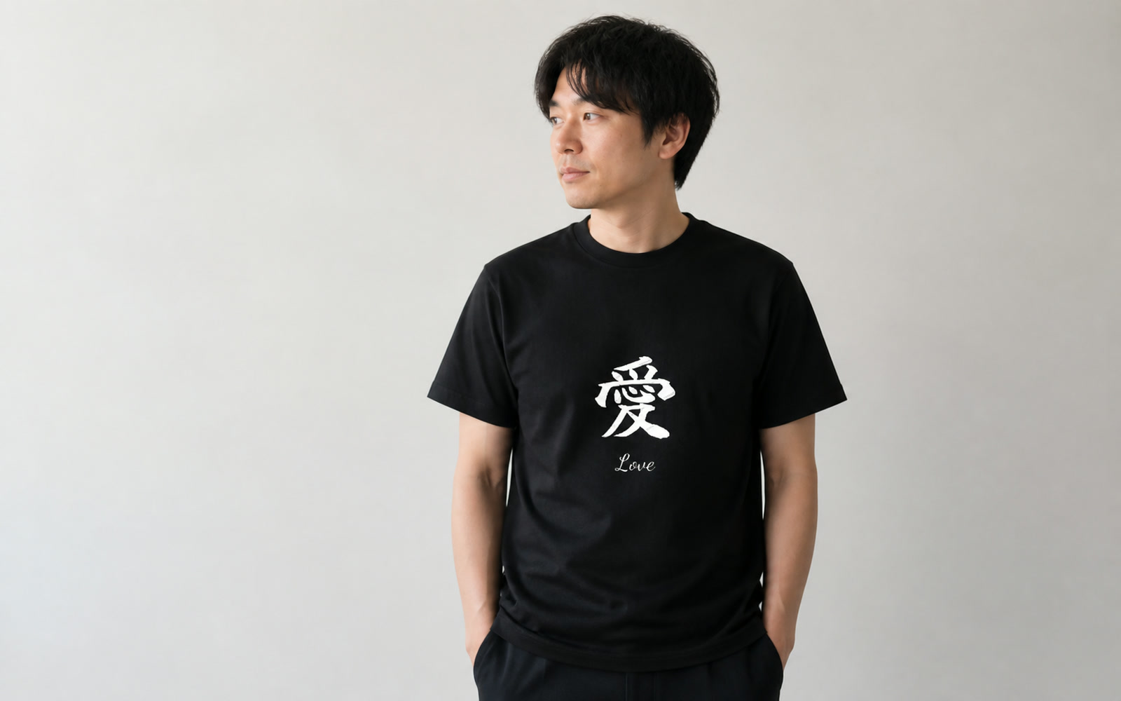 白壁の前で一文字の大判プリントTシャツを着た人物のミニマルなポートレート（字形が主役）